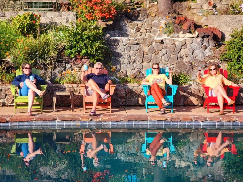 Four people sit in multicolor chairs in front of a pool cheersing