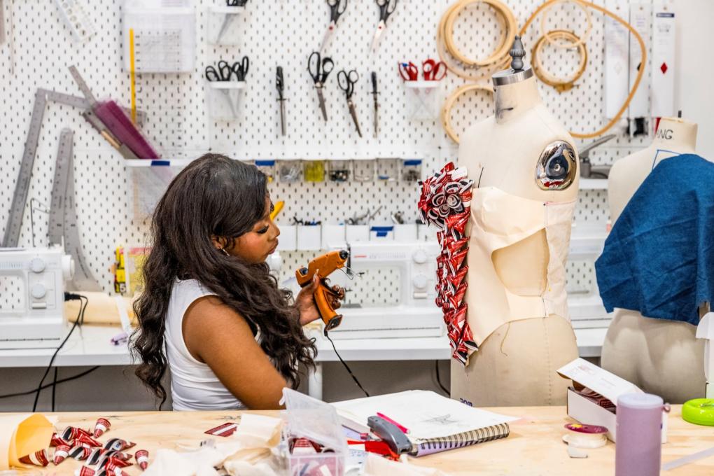 A person holding a glue gun in front of a mannequin