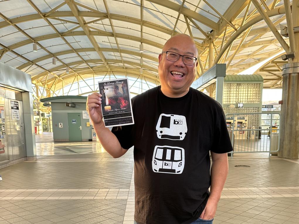 Mark Nagales smiles in a BART station with the program from his grandmother's memorial.